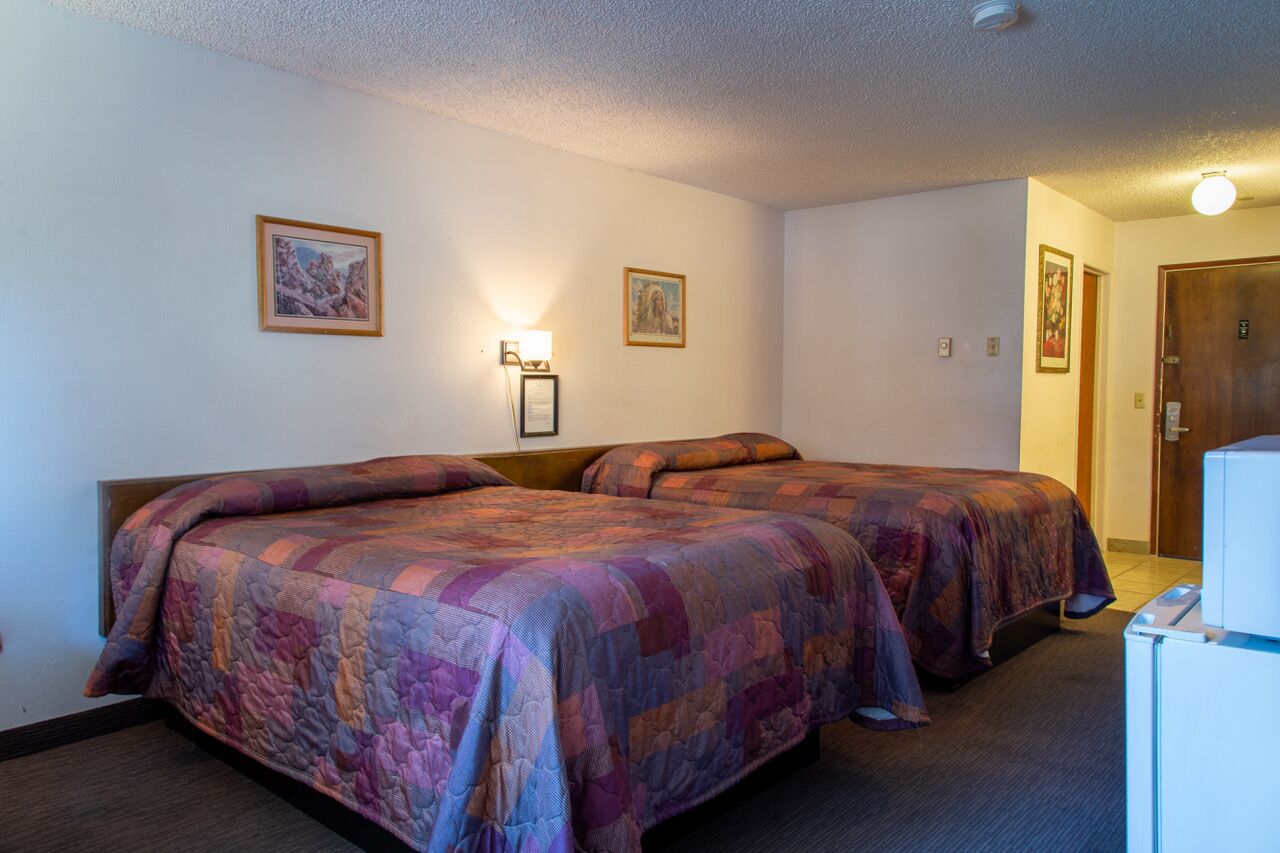 A hotel room with two beds, a nightstand with a lamp, and framed pictures on the wall.