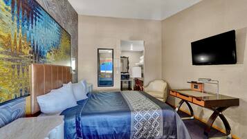 A hotel room with a large bed, a desk, a flat-screen TV, and a painting on the wall.