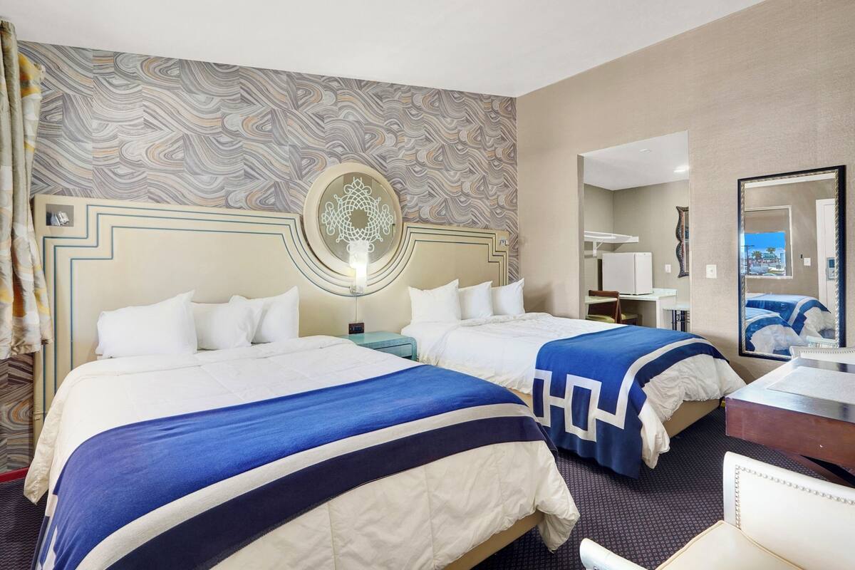A hotel room with two beds, a large mirror, and a patterned wall.