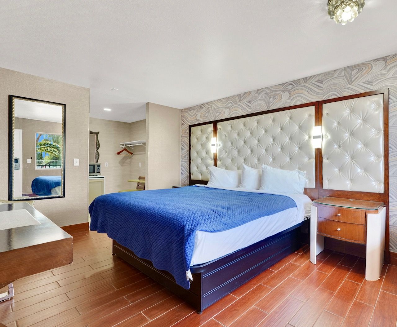Quarto de hotel com uma cama grande, mesa de cabeceira, espelho e guarda-roupa.