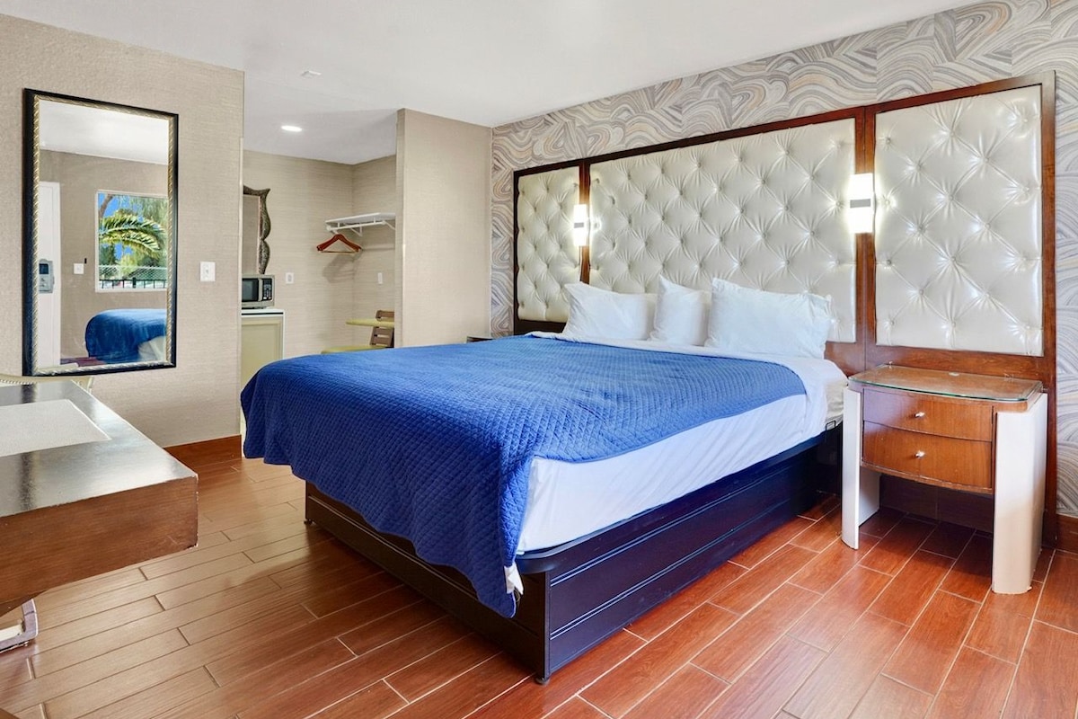 A hotel room with a bed, bedside table, mirror, and a view of the outside.