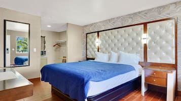 Quarto de hotel com uma cama grande, mesa de cabeceira, espelho e guarda-roupa.