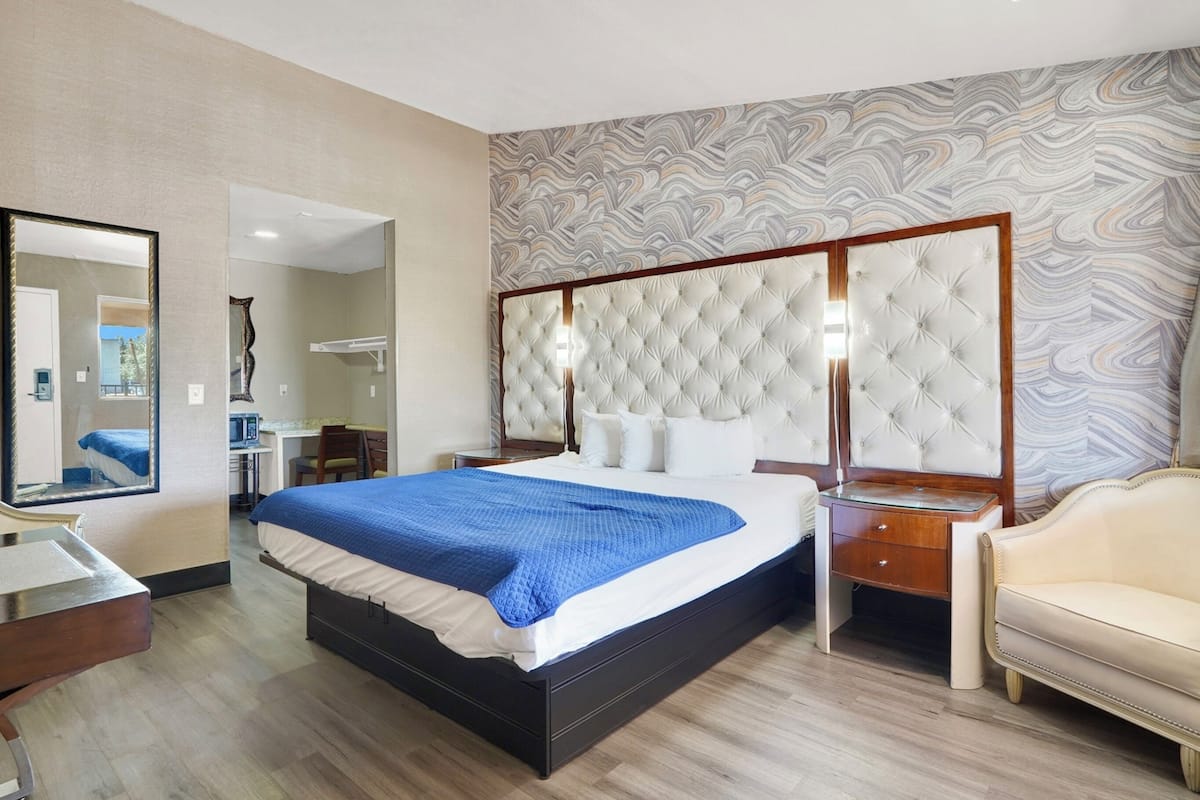 A hotel room with a large bed, a bedside table, a chair, a desk, and a mirror.