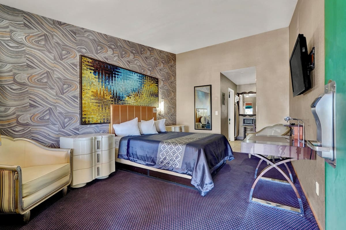 A hotel room with a large bed, a sofa, a vanity with a mirror, and a television mounted on the wall.