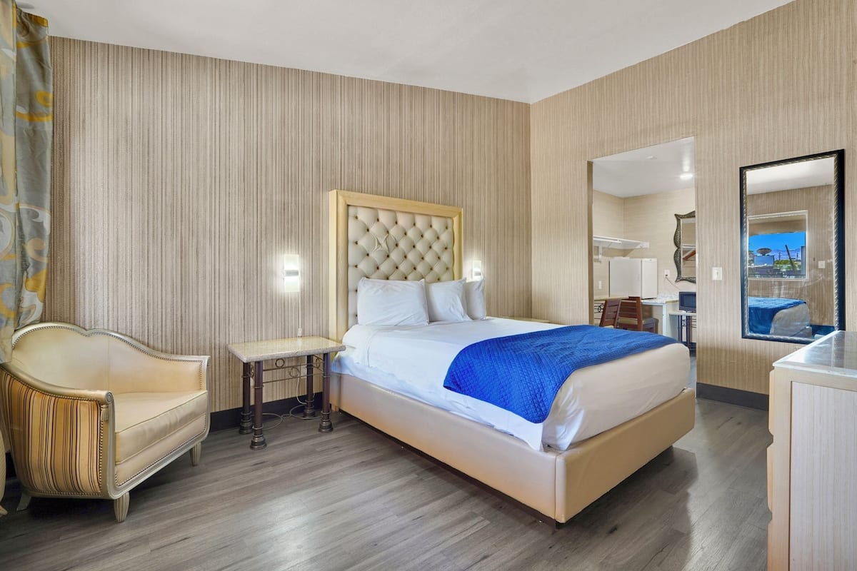 A hotel room with a large bed, a desk, a chair, and a mirror.