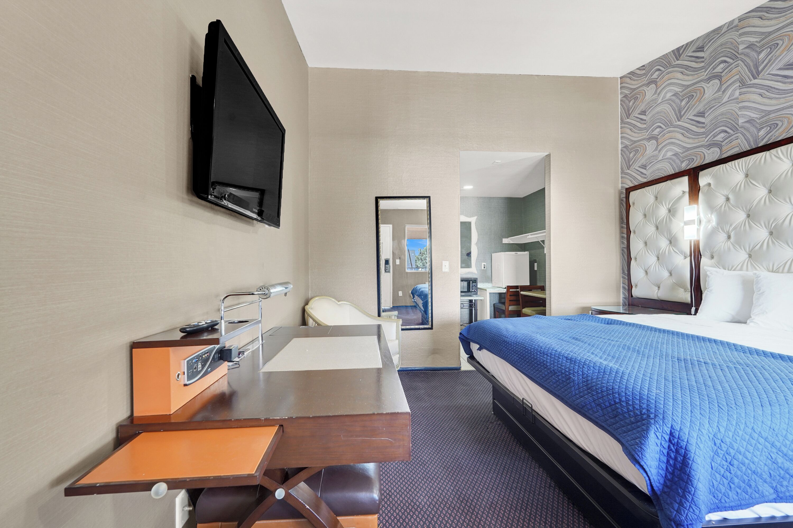 A hotel room with a bed, a desk with a chair, a television mounted on the wall, and a mirror.