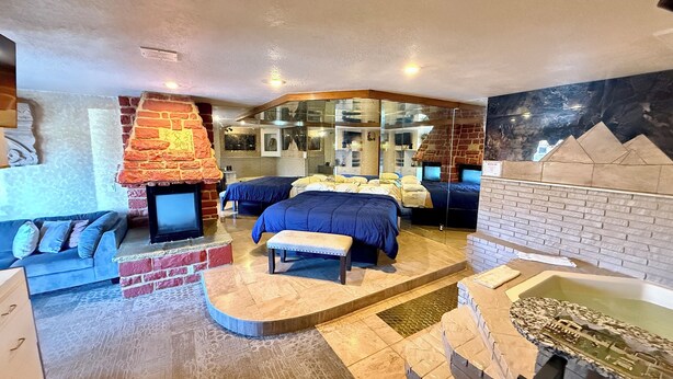 Ein Hotelzimmer mit Kamin aus Backsteinen, zwei Betten, einer Couch und einem kleinen Billardtisch.