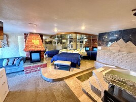 Una habitación de hotel con chimenea de ladrillo, dos camas, un sofá y una mesa de billar pequeña.