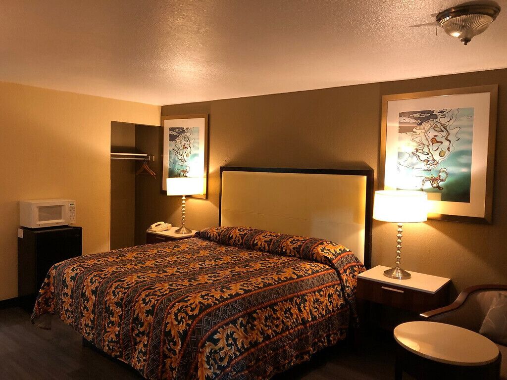 A hotel room with a large bed, two bedside lamps, a microwave, a telephone, and two framed pictures on the wall.