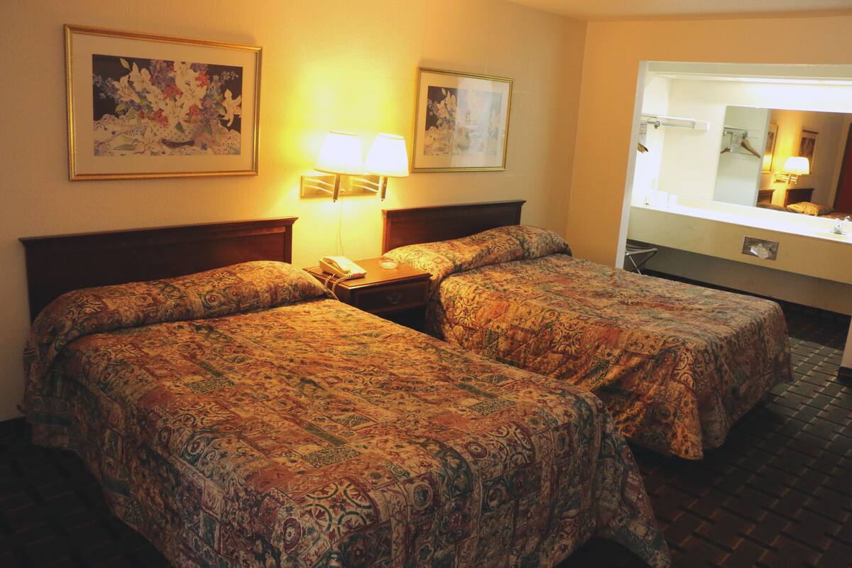Une chambre d’hôtel avec deux lits, une table de chevet avec une lampe, un miroir et deux tableaux encadrés au mur.