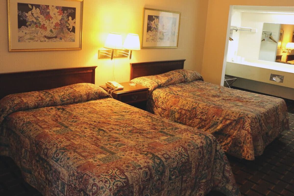 Une chambre d’hôtel avec deux lits, une table de chevet avec une lampe et un grand miroir.