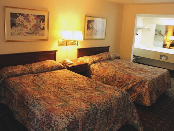 Quarto de hotel com duas camas, uma mesa de cabeceira com abajur e um espelho grande.