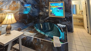 Ein Badezimmer mit Marmorwand, einer Badewanne, einem Fernseher und einem Tisch mit einer Lampe.