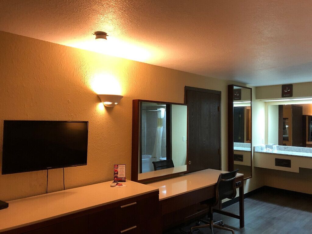 Habitación de hotel con televisor de pantalla plana grande, escritorio con silla y espejo amplio.