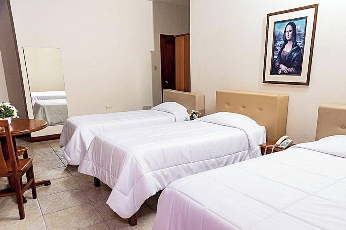 A hotel room with two beds, a bedside table with a phone, a framed artwork on the wall, and a wooden chair.