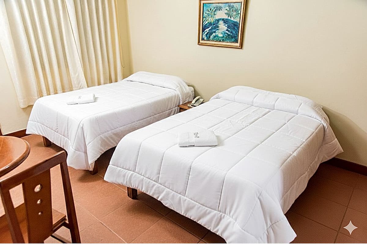 Two single beds with white bedding, a wooden chair, a telephone, and a painting of a tropical scene on the wall.