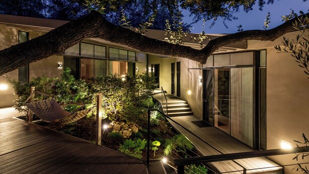 A modern building with a wooden deck, a staircase, and a garden area with plants and a hammock. - Frame Hotel - Treehouse (Austin)