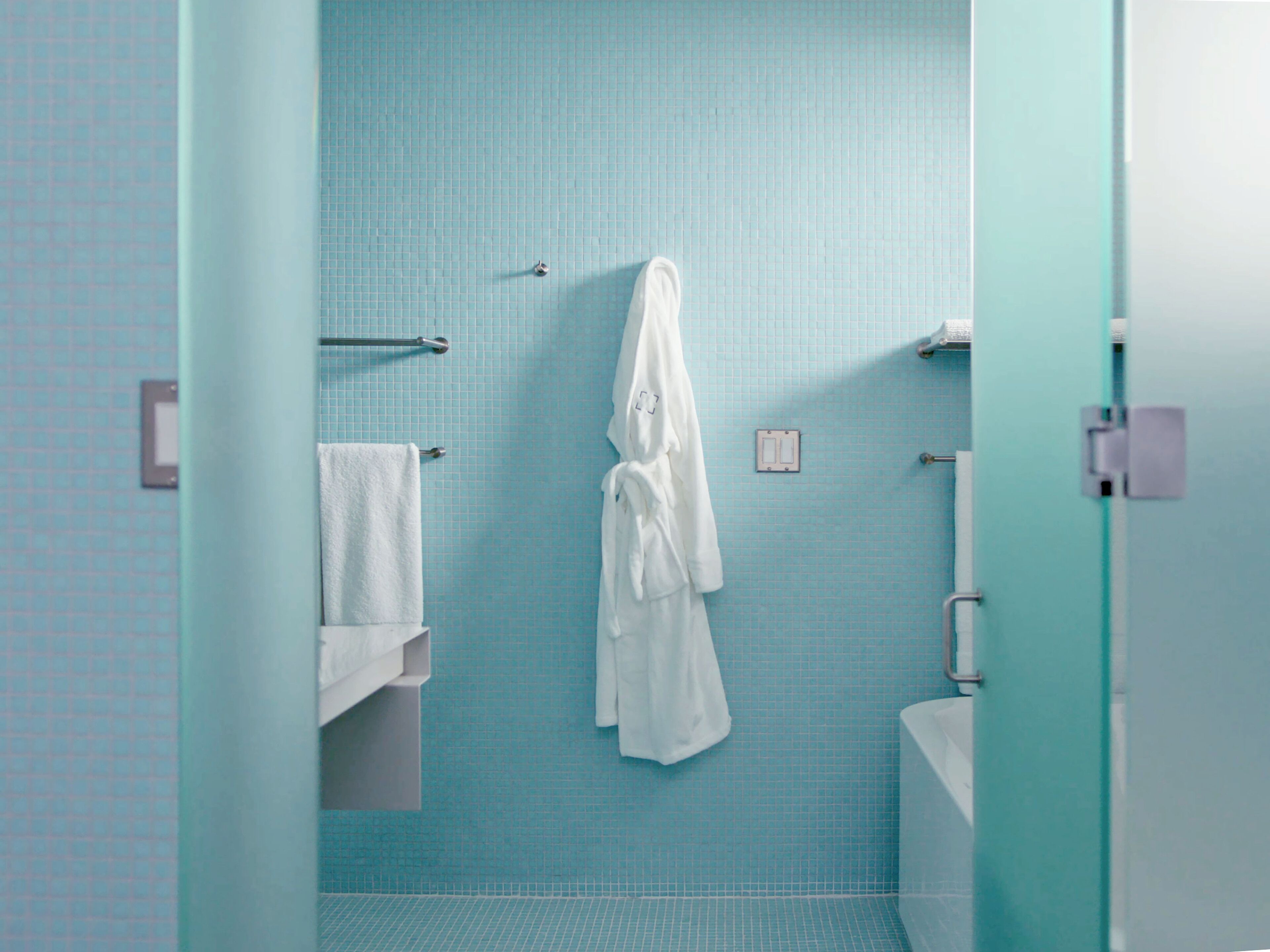 Ein Badezimmer mit blauen Fliesen, einem weißen Handtuch auf einem Halter und einem weißen Bademantel an einem Haken.