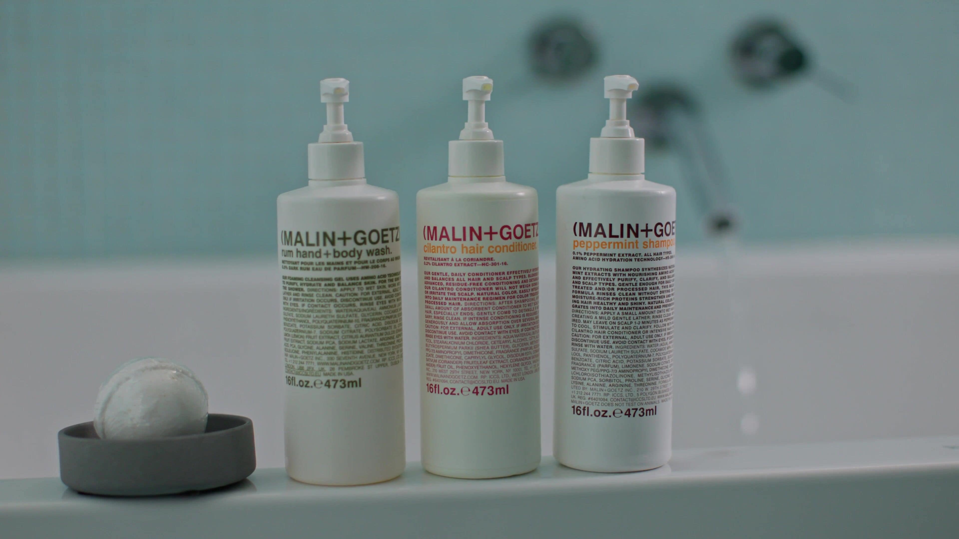 Three bottles of MALIN+GOETZ hair conditioner on a bathroom counter.