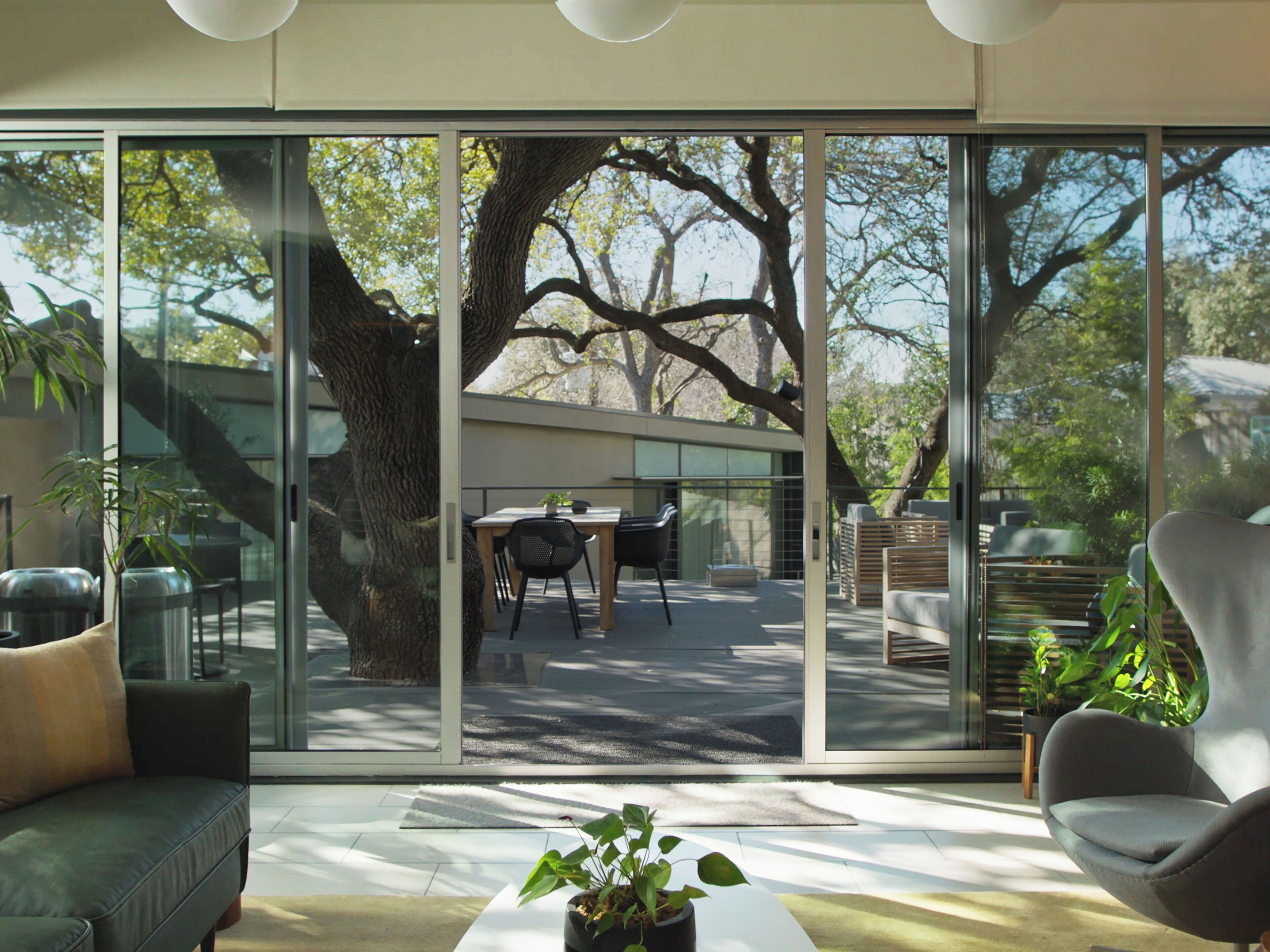 A modern living room with a glass wall, a sofa, a coffee table, and a dining area with chairs and a table.