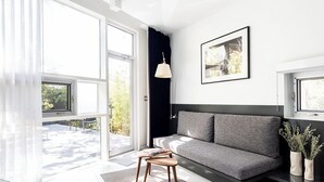 A modern living room with a grey sofa, a small wooden table, and a large window providing a view of the outdoors. - Frame Hotel - Treehouse (Austin)