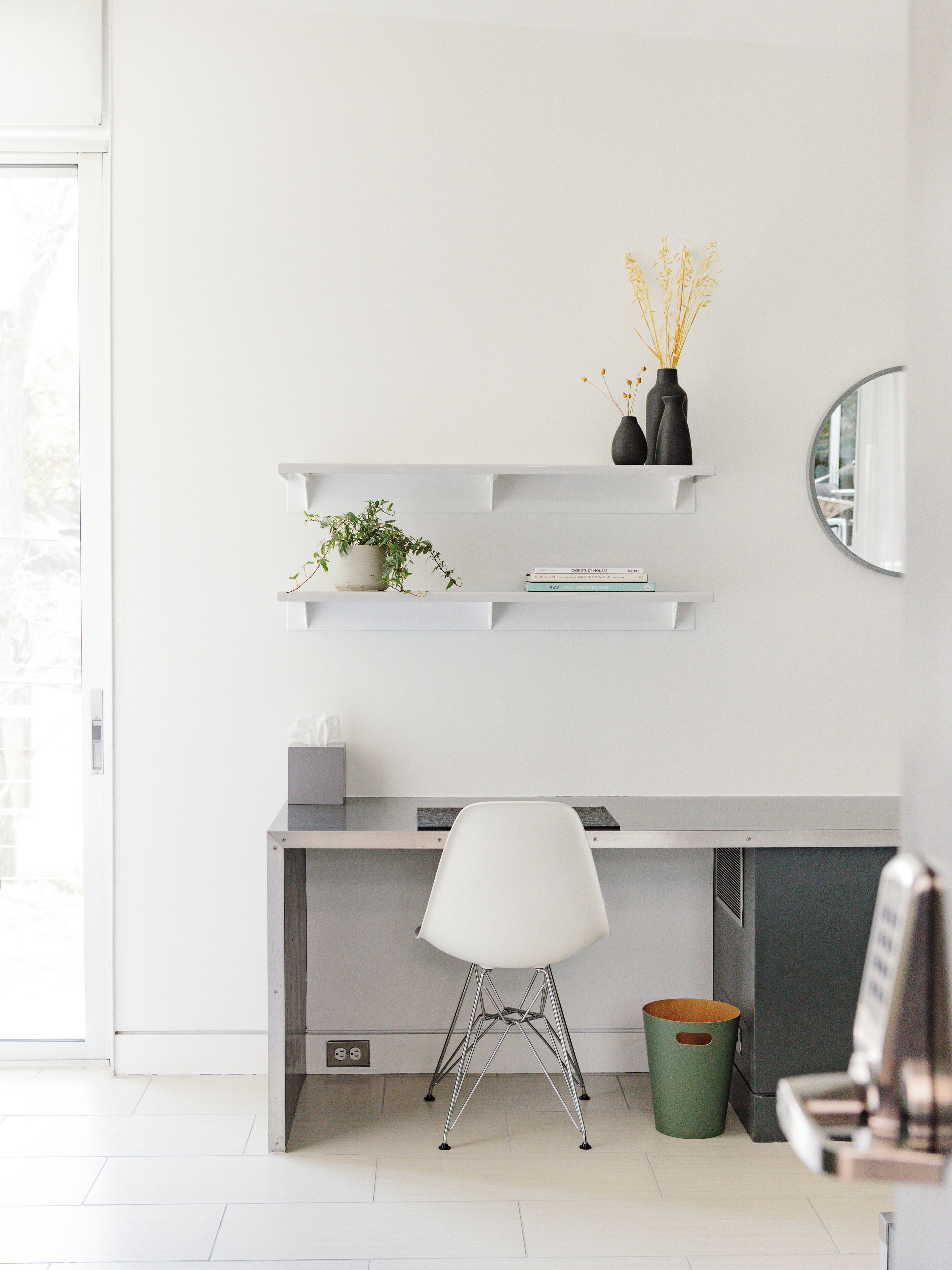 Een moderne kantoorruimte met een bureau, stoel, plantenbakken en een spiegel.
