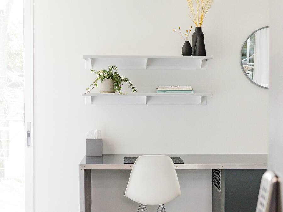 Un espace de bureau moderne comprenant un bureau, une chaise, des étagères avec des plantes et un miroir.