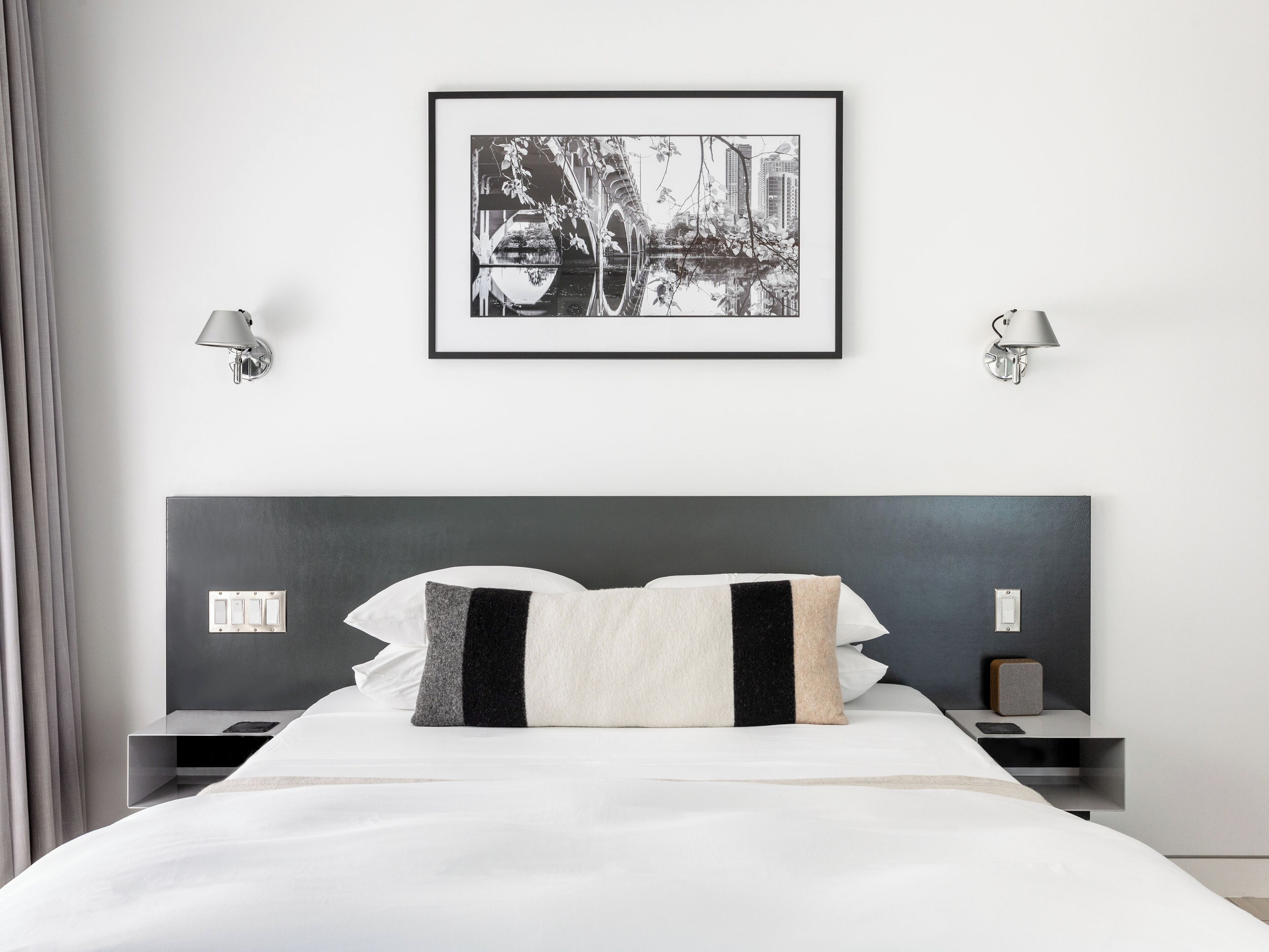 Une chambre d’hôtel moderne avec un grand lit, deux tables de chevet, un tableau encadré au mur et deux lampes fixées au mur.