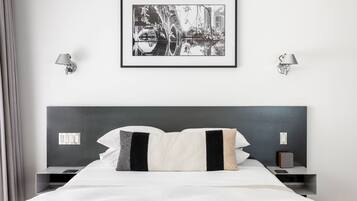 Une chambre d’hôtel moderne avec un grand lit, deux tables de chevet, un tableau encadré au mur et deux lampes fixées au mur.