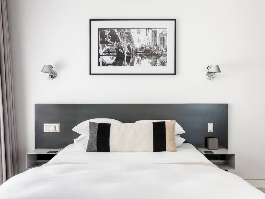 Une chambre d’hôtel moderne avec un grand lit, deux tables de chevet, un tableau encadré au mur et deux lampes fixées au mur.