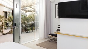 A modern hotel room with a large TV, sliding glass doors to a balcony, and a small dining area. - Frame Hotel - Treehouse (Austin)