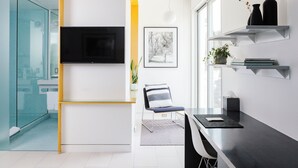 A modern living room with a TV, a framed picture, a chair, and a dining area with a table. - Frame Hotel - Treehouse (Austin)