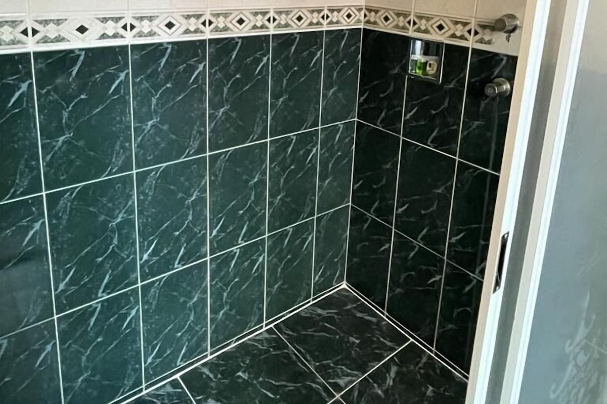A shower area with dark marble tiles and a white decorative border.