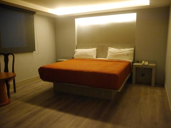 Un dormitorio con cama, mesita de noche, una silla y ventana con persianas.