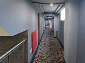 A long hallway with patterned carpet, blue walls, and a red door.