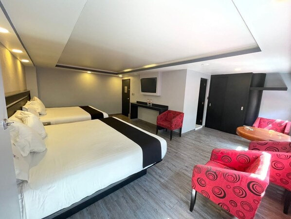 A hotel room with two beds, a desk, a TV, and red patterned chairs.