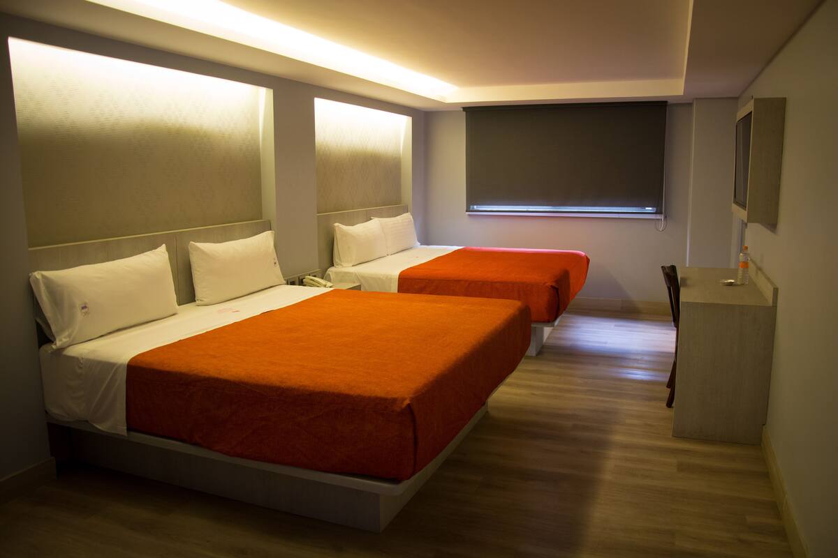 Habitación de hotel con dos camas, un escritorio pequeño y una ventana con persianas.