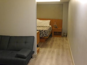 A compact hotel room with a bed, bedside table, and a sofa.