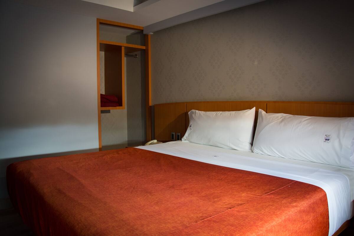 Una habitación de hotel con una cama, un armario de madera y un papel tapiz estampado.