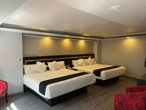 A hotel room with two beds, a red chair, and a wooden floor.