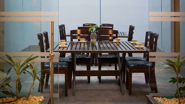 Un espace bar avec une table et des chaises en bois, une enseigne au-dessus indiquant « BAR », et des plantes en pot de chaque côté.