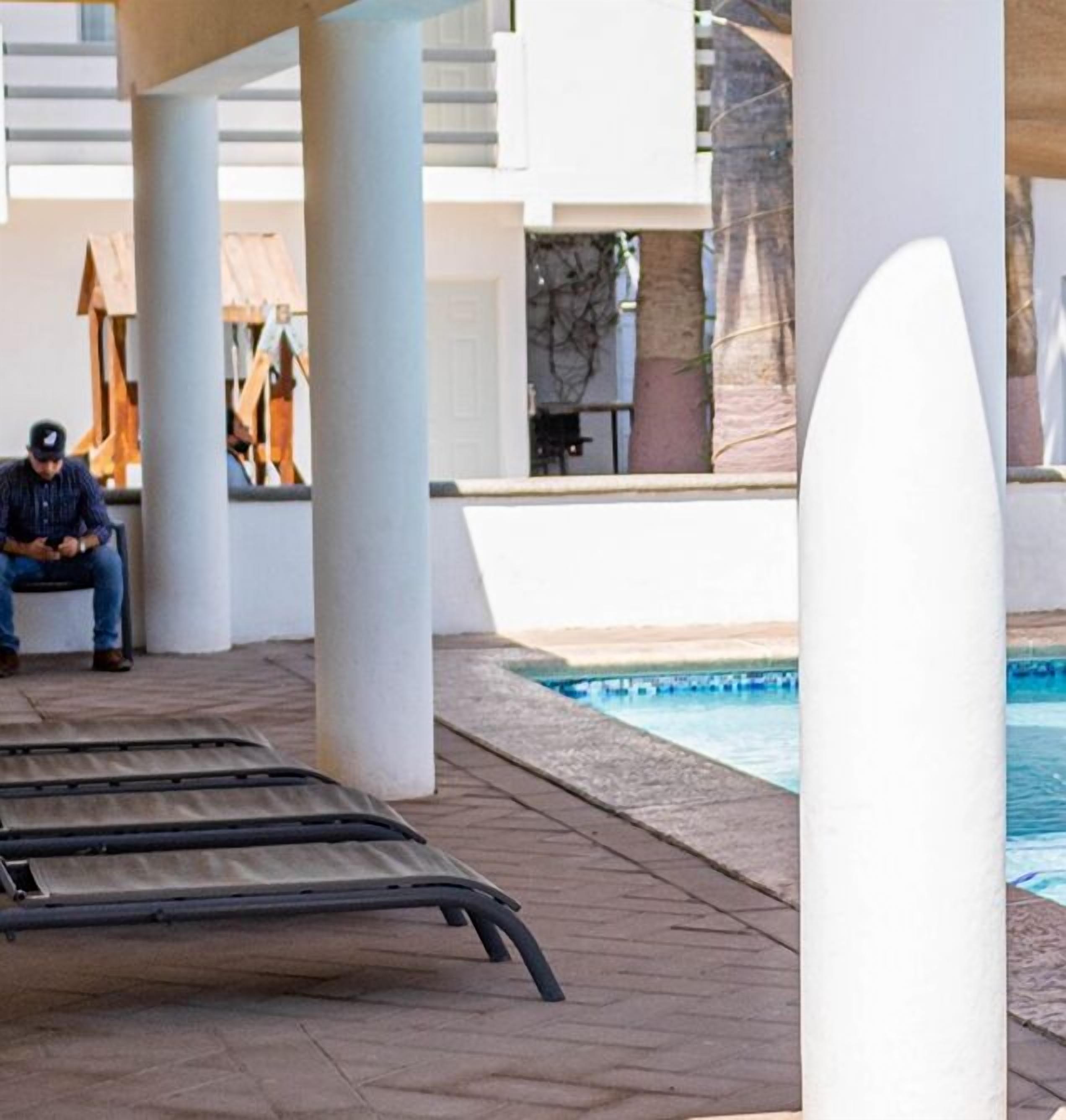 Area piscina con lettini, un uomo seduto su una panchina e una piscina.
