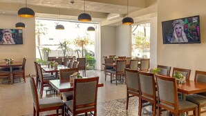 Un vaste espace dédié à la salle à manger, avec de nombreuses tables et chaises, de grandes fenêtres et des luminaires suspendus fixés au plafond.