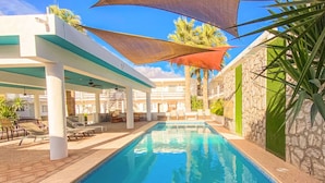 Une piscine entourée de murs en pierre et de palmiers, avec des chaises longues et des parasols.