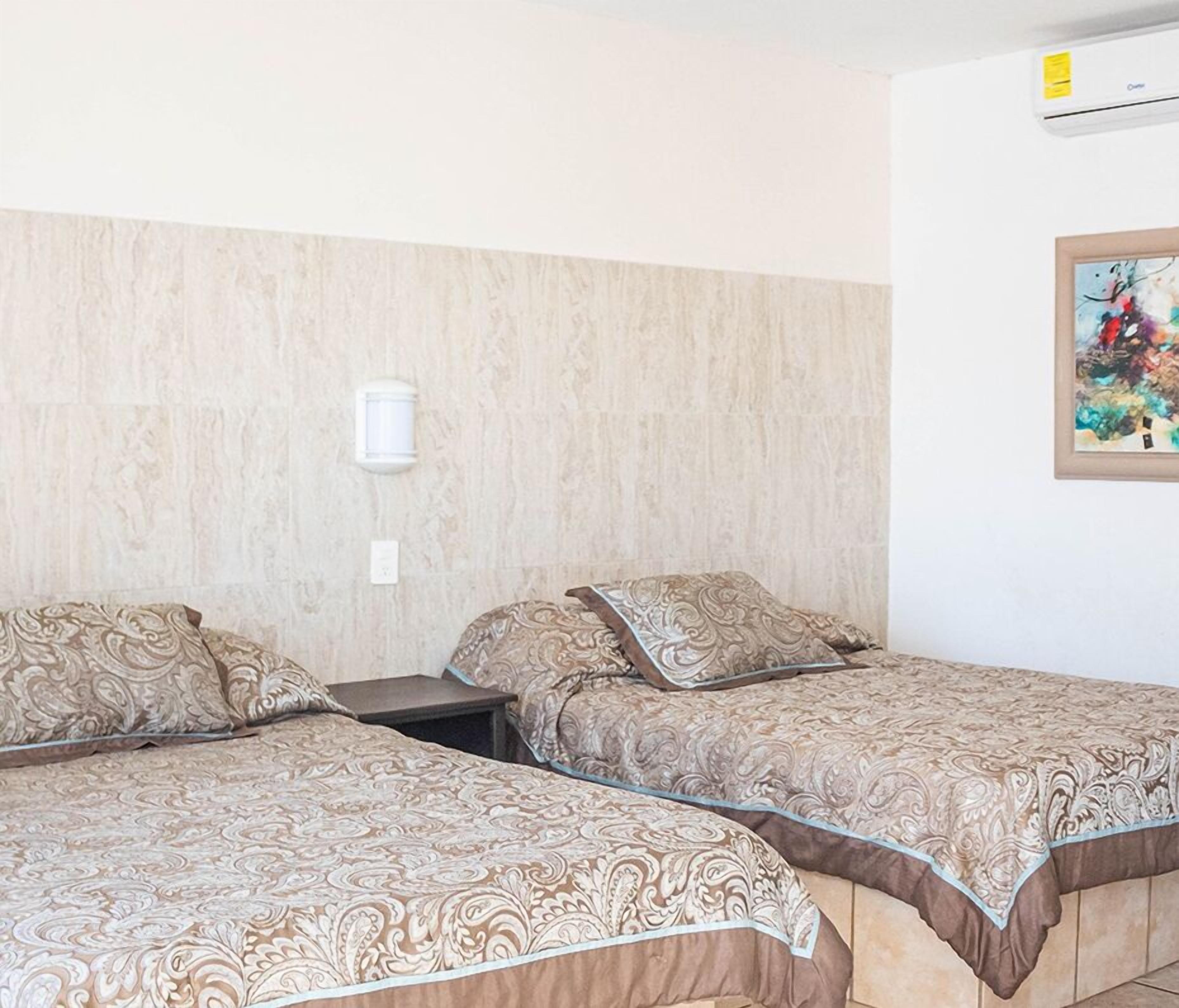 A hotel room with two beds, a wall-mounted air conditioner, and a painting on the wall.