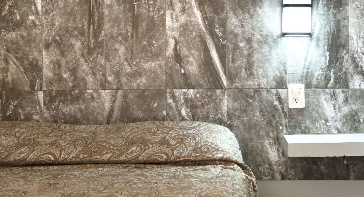 A bedroom with a bed, a marble wall, a nightstand, and a window.