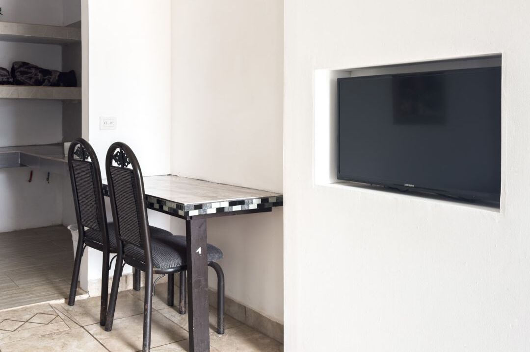 A dining area with a table and chairs, a built-in TV on the wall, and a shelf with folded clothes.