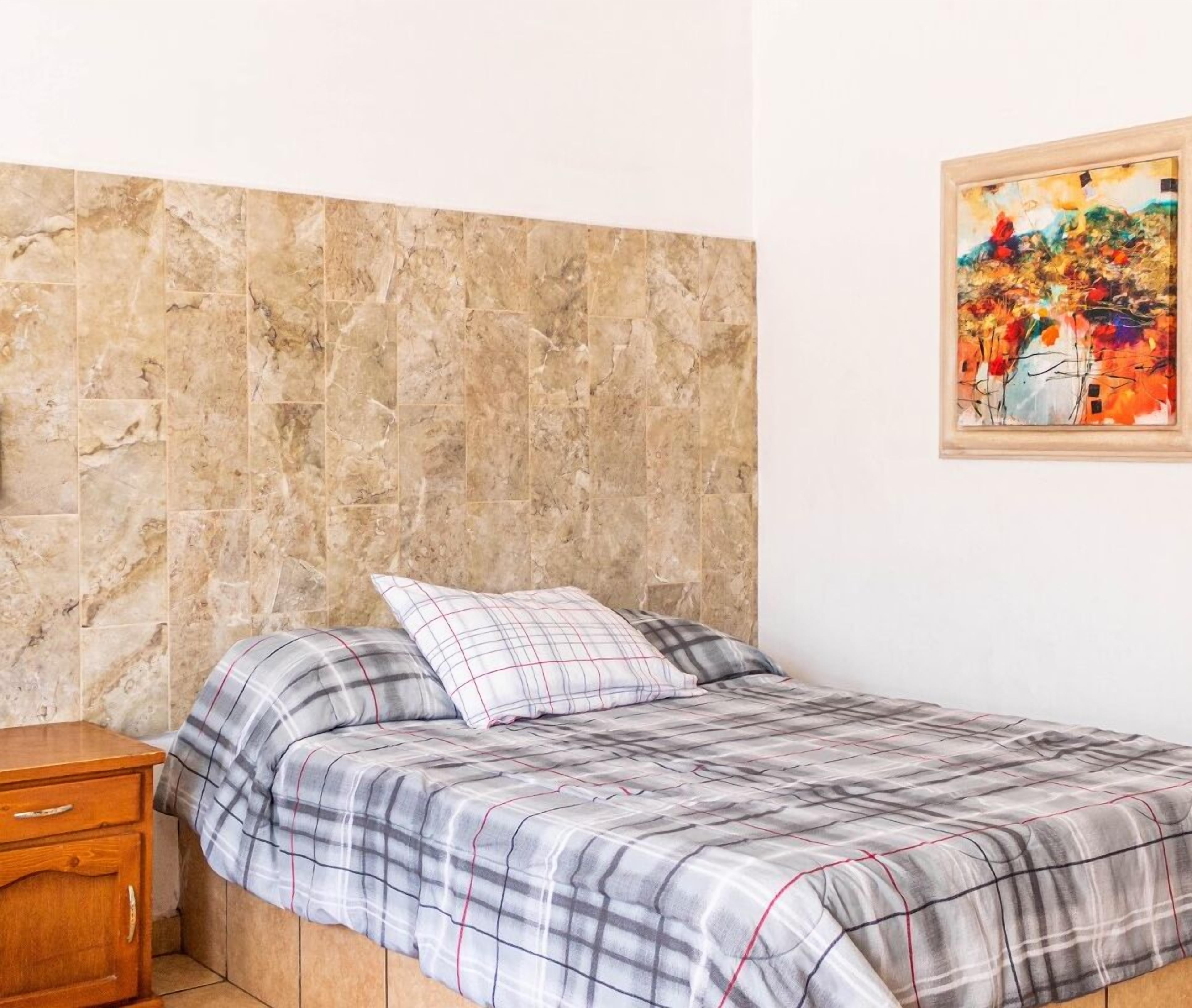A bedroom with a bed, a nightstand, a marble headboard, and a colorful abstract painting on the wall.