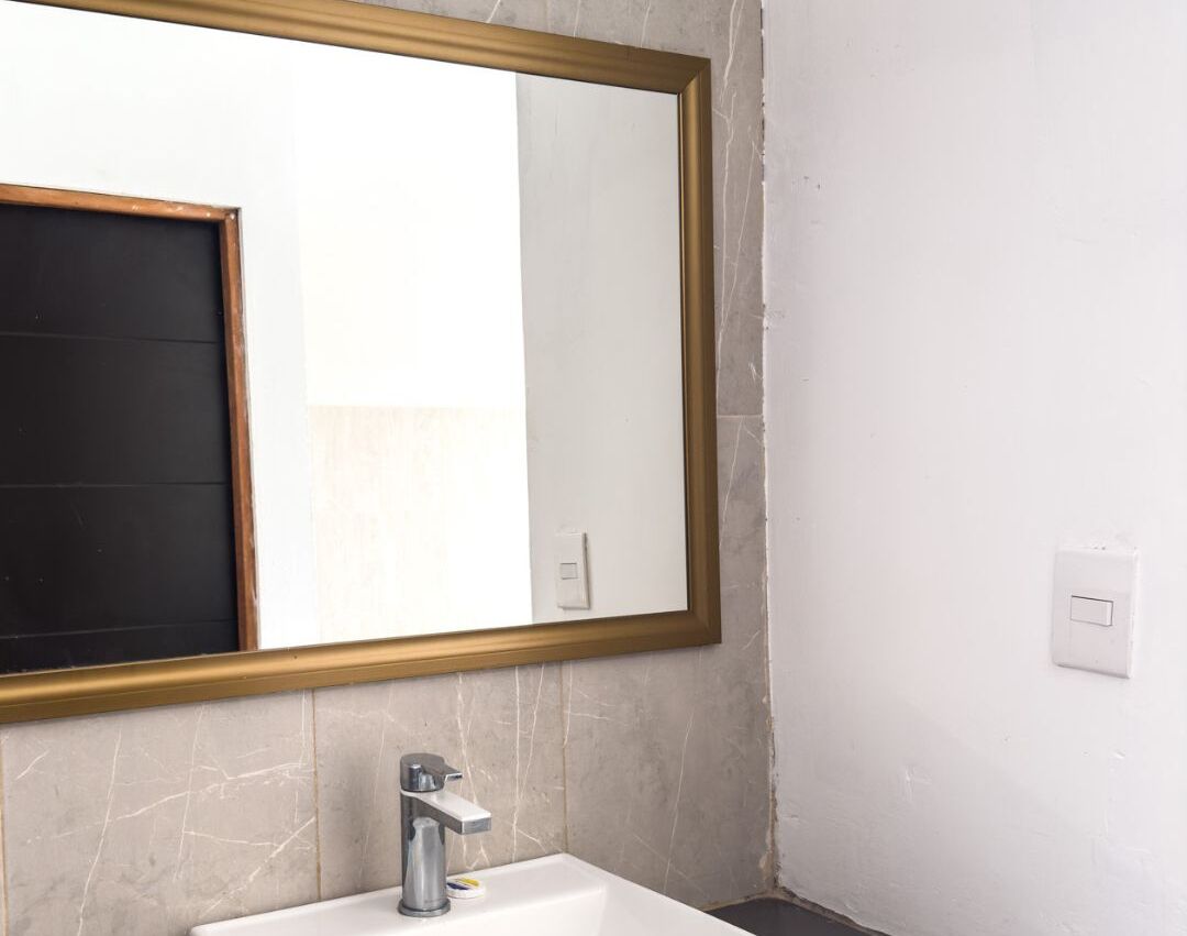A bathroom with a large mirror, a sink, and a light switch on the wall.