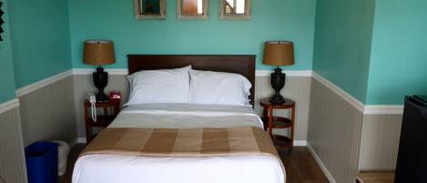 A neatly made bed in a room with teal walls, two bedside lamps, and three framed mirrors on the wall.